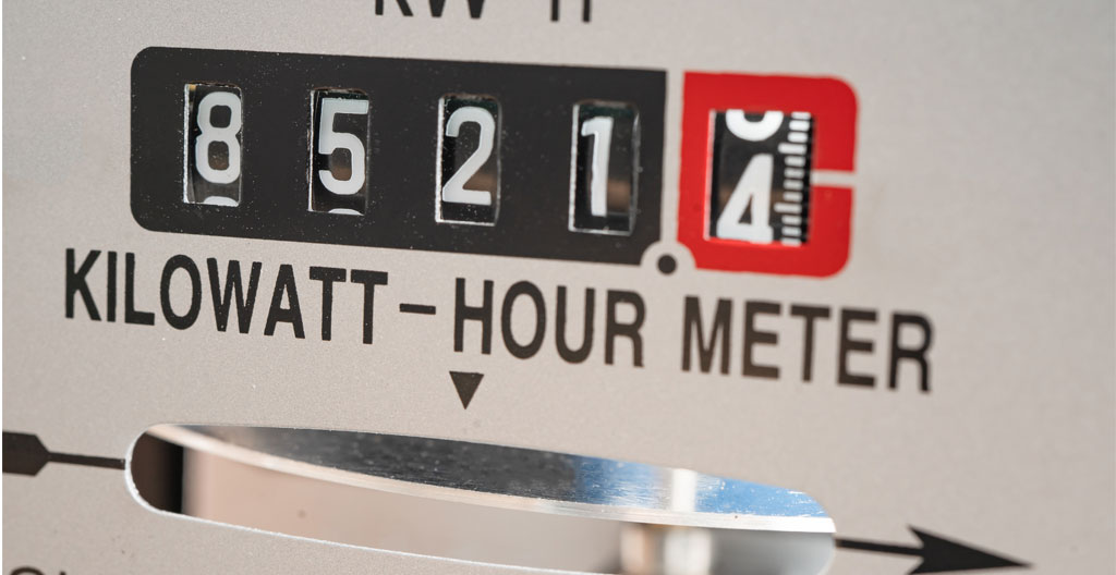 Un compteur électrique triphasé dans un local technique industriel avec câbles et armoire électrique en arrière-plan